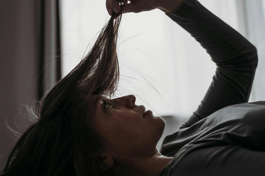 Mujer observando la pérdida de densidad y grosor de su cabello frente a una ventana, representando los cambios capilares en la perimenopausia.